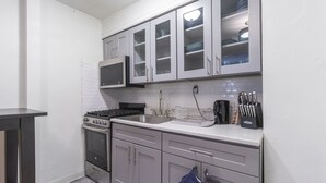 A compact kitchen with grey cabinets, a microwave, stove, sink, and a knife block. - Amazing 2 BR on Upper East Side NYC (New York)