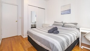 Een slaapkamer met een bed, nachtkastje, spiegel en een schilderij aan de muur.
