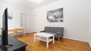 Een moderne woonkamer met een flatscreen televisie, een grijze bank, een witte salontafel en een stadslandschap op de muur.