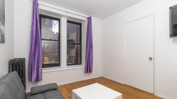 A room with a grey sofa, a white table, and two windows with purple curtains.