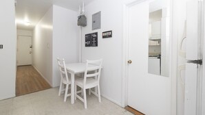 A small, white-walled room with a white table and chairs, a door, and a wall-mounted light fixture.