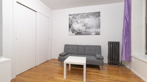 A room with a grey sofa, a white table, a radiator, and a window with purple curtains.