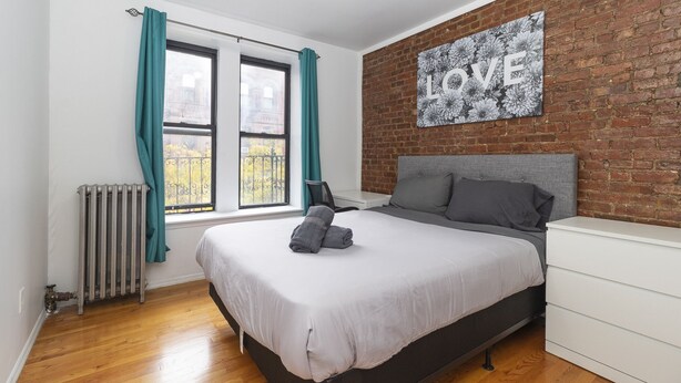 A modern bedroom with a large bed, a brick wall, and a "LOVE" artwork. - Spacious Two BR Apartments in Yorkville Upper East NYC (Manhattan)