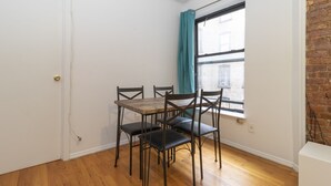 A dining area with a wooden table and four chairs, a window with a curtain, and a brick wall. - Spacious Two BR Apartments in Yorkville Upper East NYC (Manhattan)