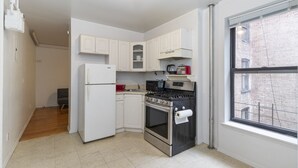 A compact kitchen with white cabinets, a stainless steel stove, and a refrigerator. - Spacious Two BR Apartments in Yorkville Upper East NYC (Manhattan)
