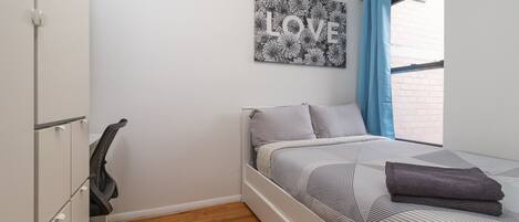A bedroom with a bed, a desk, and a chair. There is a window with blue curtains and a picture on the wall that says "LOVE".