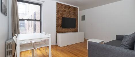 A modern living room with a white table, grey sofa, and a brick wall.