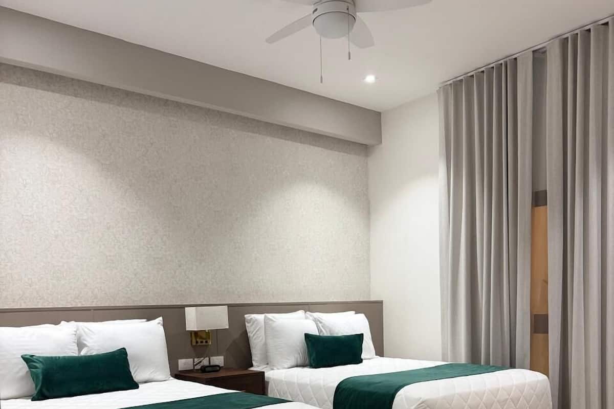 A hotel room with two beds, a ceiling fan, a desk, and a chair.