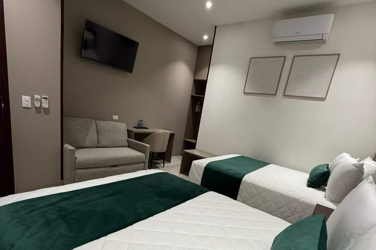 A hotel room with two beds, a TV, an air conditioner, and a desk with a chair.
