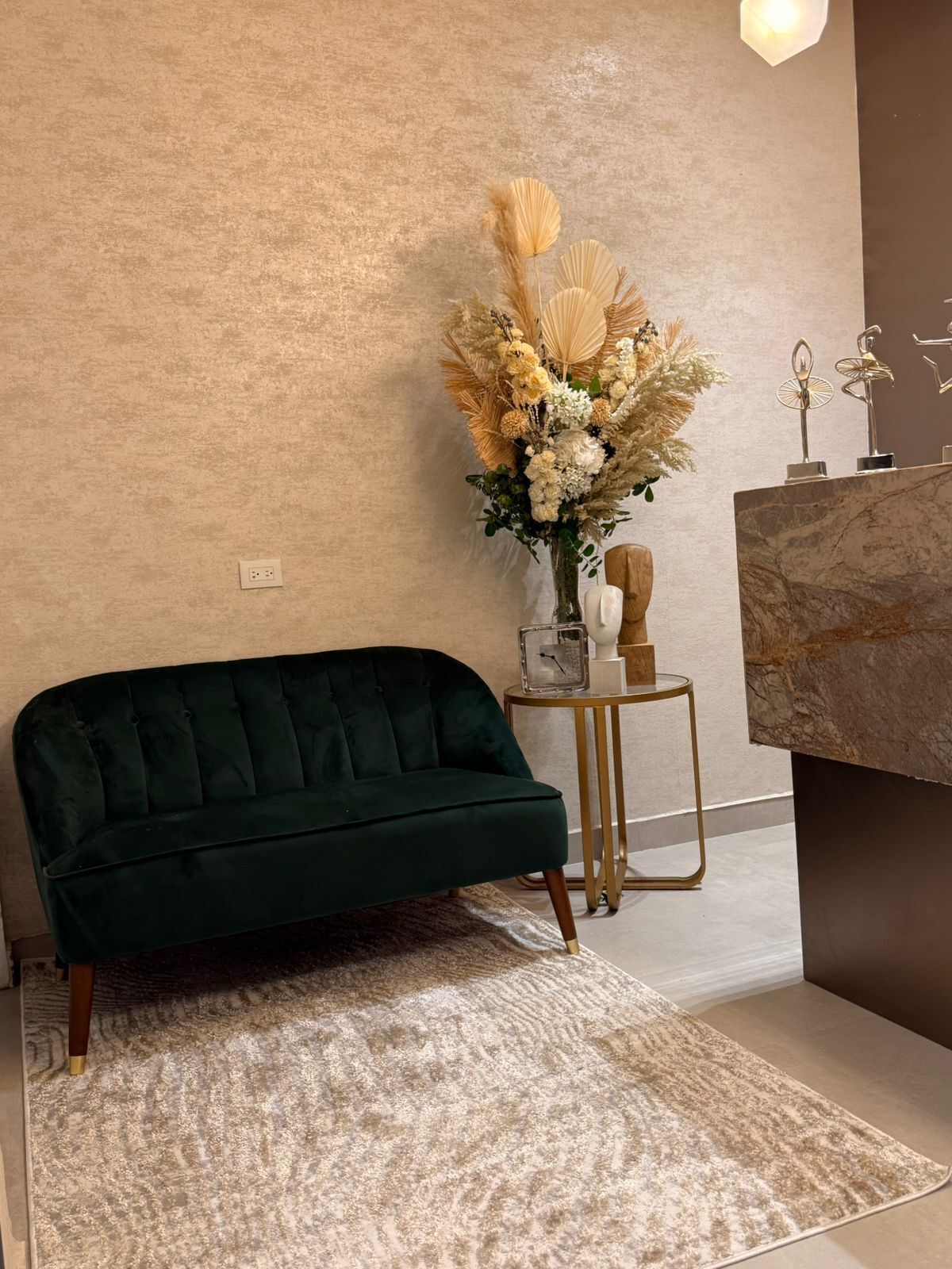 A green sofa, a decorative vase with flowers, a small table with a lamp, and a marble countertop.