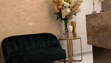 A green sofa, a decorative vase with flowers, a small table with a lamp, and a marble countertop.