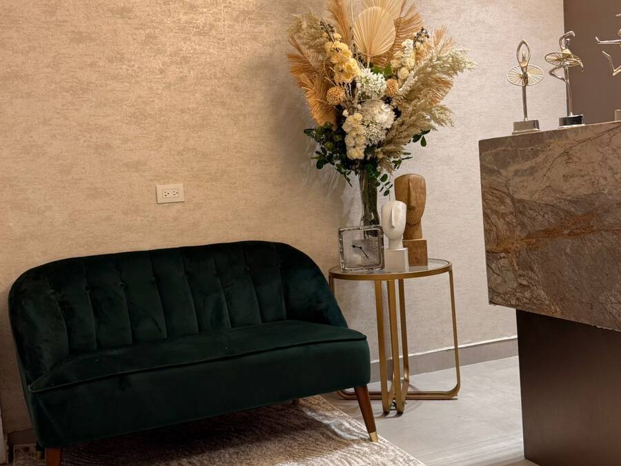 A green sofa, a decorative vase with flowers, a small table with a lamp, and a marble countertop.