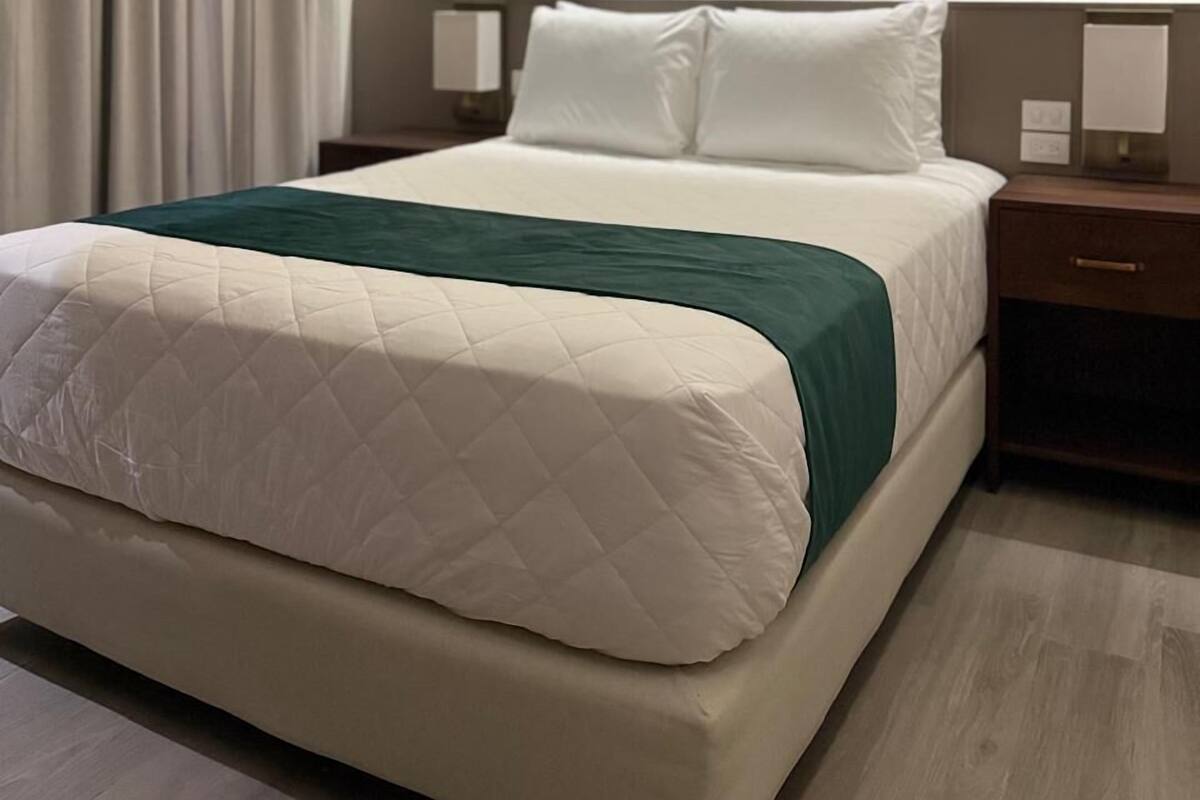 A modern hotel room with a large bed, a nightstand, and a wall-mounted light fixture.