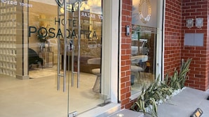 Entrada de hotel con puerta de vidrio, un cartel sobre la puerta y un muro de ladrillo.