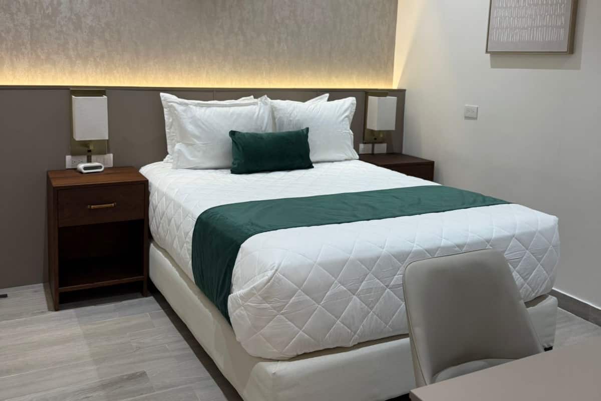 A modern bedroom with a bed, bedside tables, a desk, and an air conditioning unit.