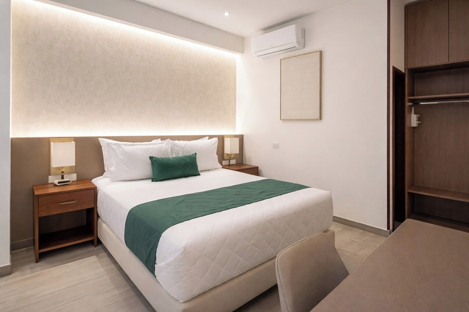 A hotel room with a bed, bedside tables, a desk, and an air conditioning unit.
