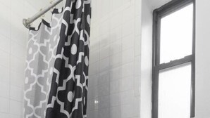 Ein Badezimmer mit Toilette, einer Duschvorhang mit Schwarzweißmuster und einem Fenster über der Toilette.