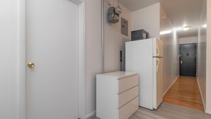 Ein schmaler Flur mit einer weißen Tür, einem weißen Schrank, einem Kühlschrank und Holzboden.