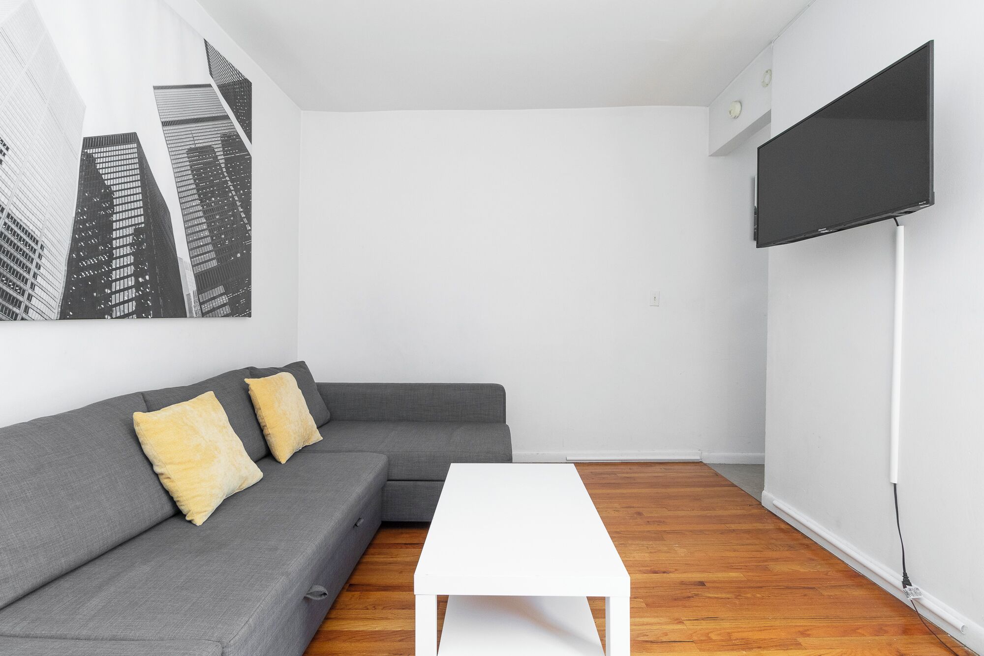 A modern living room with a grey sofa, a white coffee table, and a large black TV screen.