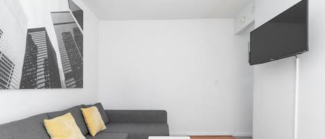 A modern living room with a grey sofa, a white coffee table, and a large black TV screen.