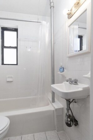 Une salle de bain avec une baignoire, un lavabo, une fenêtre et un miroir.