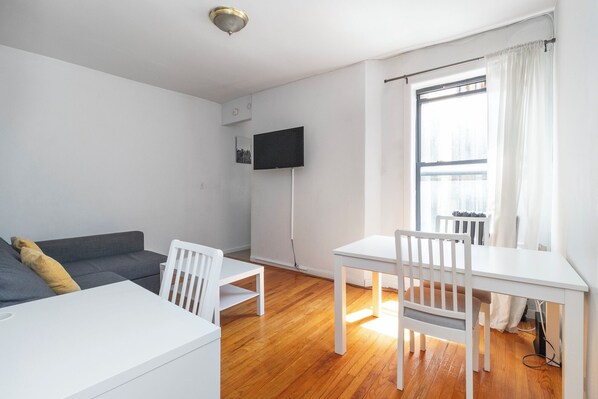 Un salon moderne et minimaliste, avec un canapé gris, des chaises blanches, une table blanche et une grande fenêtre agrémentée de rideaux.