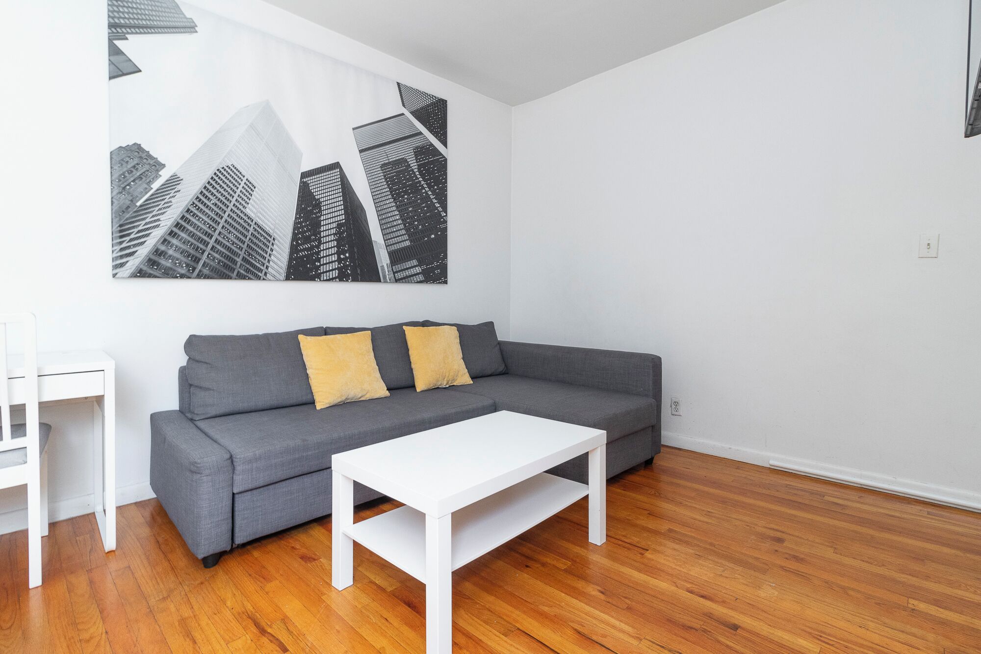 A modern living room with a grey sofa, two yellow cushions, a white coffee table, and a cityscape painting on the wall.
