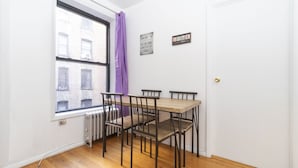 A small dining area with a wooden table and four chairs, a window with a view of buildings, a radiator, and a door.
