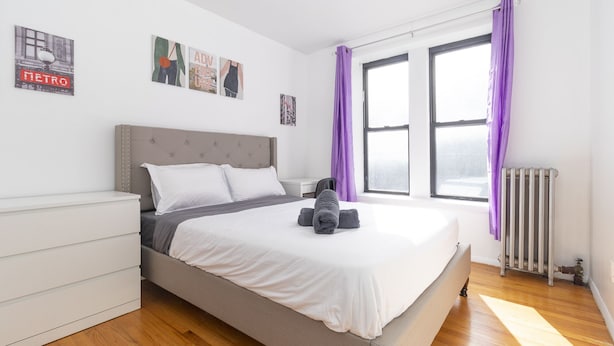 A bedroom with a bed, a radiator, and a window with purple curtains.