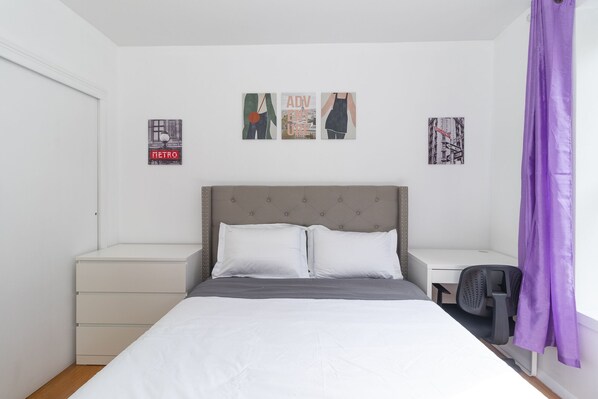 A bedroom with a bed, two bedside tables, a chair, and a purple curtain.