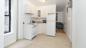 A compact kitchen with white cabinets, a stove, a refrigerator, and a microwave.