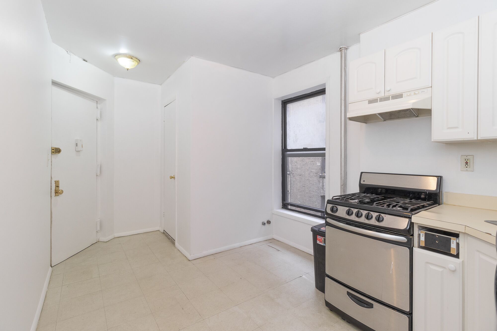 A small, white kitchen with a gas stove, oven, and white cabinets.