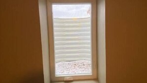Ein kleines Fenster mit horizontalen Jalousien in einem Raum mit orangen Wänden.