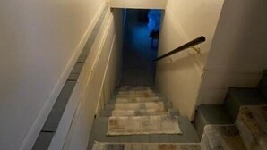 Eine enge Treppe mit Handlauf, Teppichstufen und einer Leuchte am oberen Ende.