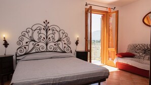 A bedroom with a bed, bedside tables, a sofa, and a balcony with a view. - Casa Sally with sea view in Macari (San Vito Lo Capo)