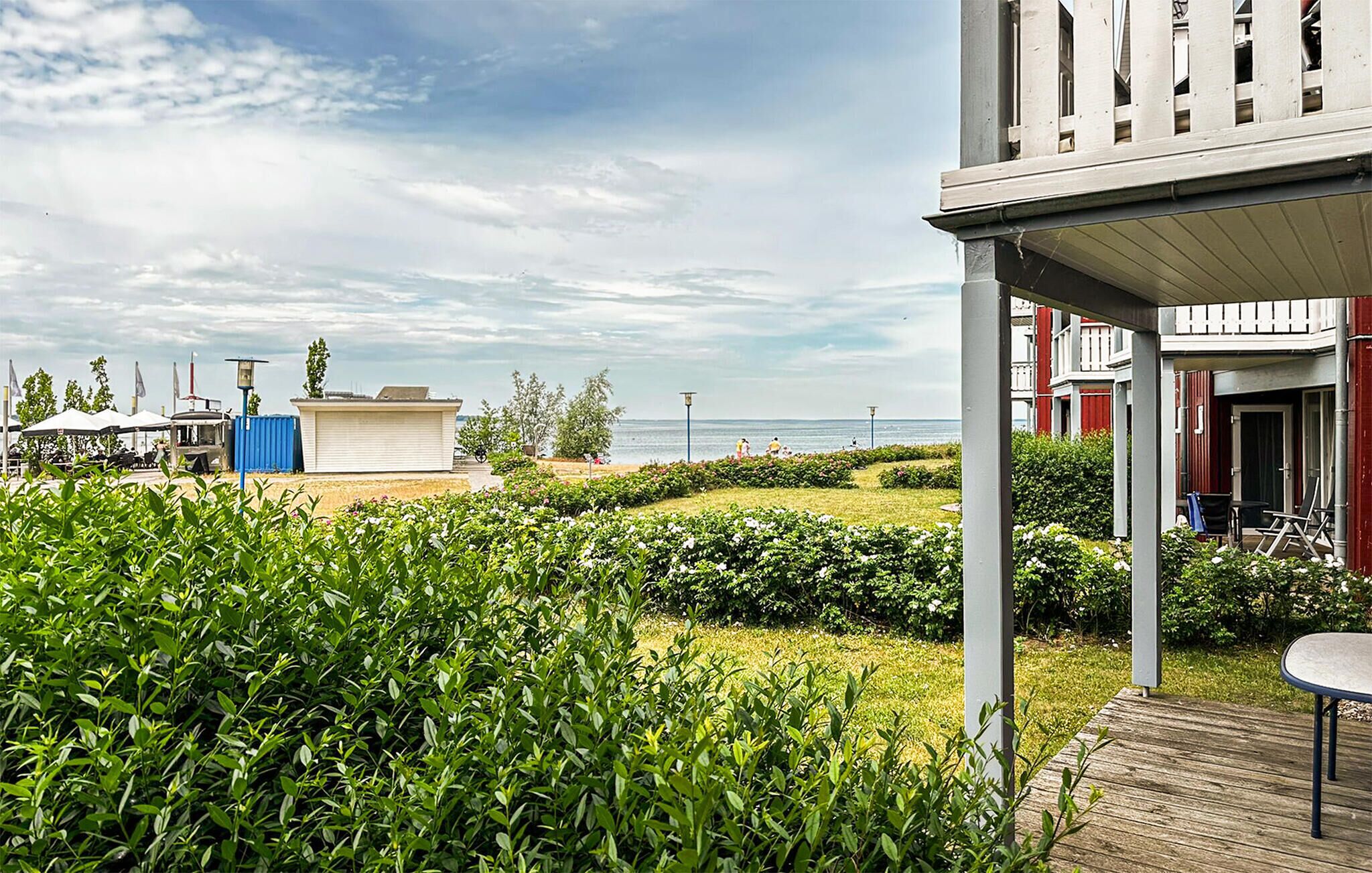 A coastal hotel with a covered outdoor seating area, a small building with a flat roof, and a view of the sea.