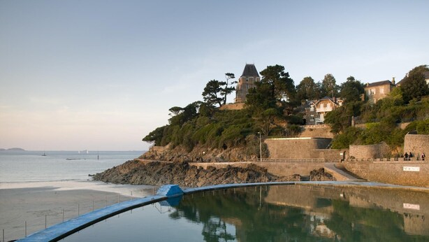 Une vue sur la côte, avec un mur de pierre, une petite tour et un bâtiment doté d’un balcon donnant sur la mer.