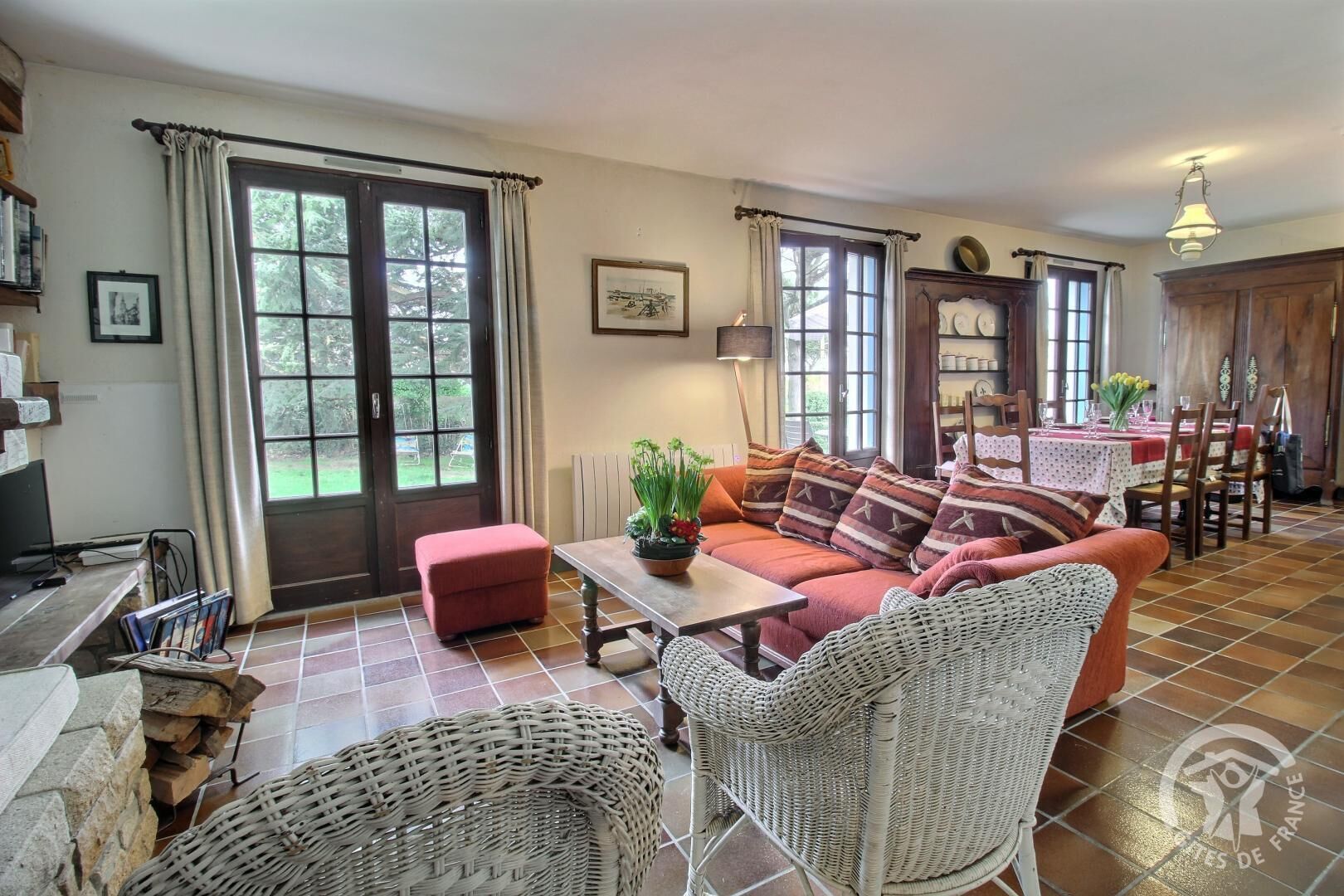 A cozy living room with a sofa, a coffee table, wicker chairs, and a dining area with a table and chairs.