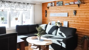 Un salón acogedor con un sofá negro y gris, una mesa de centro redonda de madera y una ventana con cortinas estampadas.