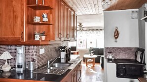 Cocina con armarios de madera, un fregadero y una estufa. Se observa un comedor con una mesa y sillas al fondo.