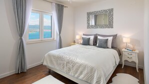 A bedroom with a large bed, a nightstand, a dresser, a mirror, and a view of the sea through a window. - Beautiful home in Mastrinka (Mastrinka)