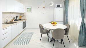 A modern kitchen with white cabinets, a microwave, and a dining area with a round table and four chairs. - Beautiful home in Mastrinka (Mastrinka)