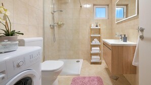 A modern bathroom with a glass shower enclosure, a built-in toilet, a sink with a mirror, and a small window. - Beautiful home in Mastrinka (Mastrinka)
