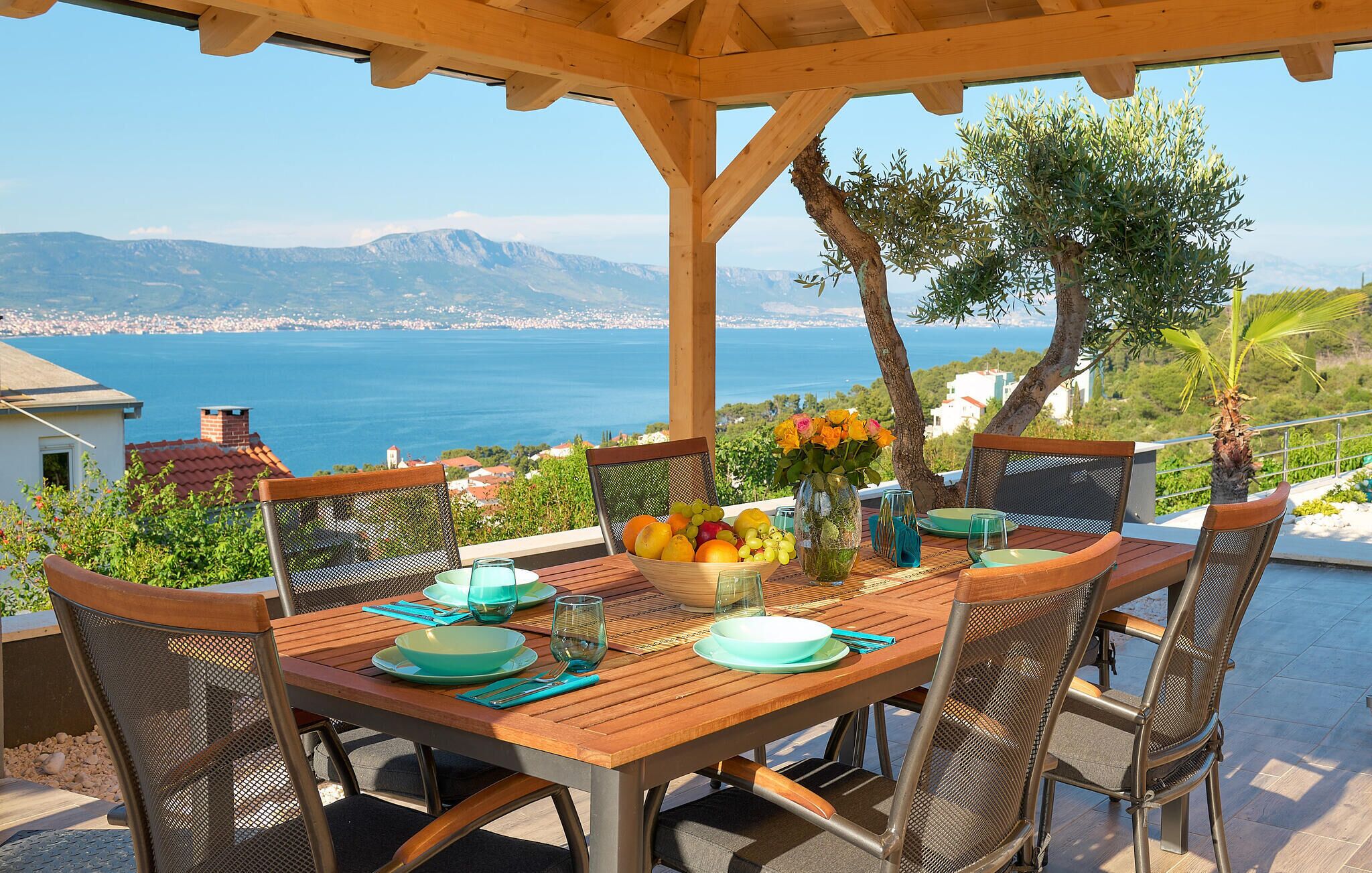 A wooden table set for dining with a view of the sea and mountains.