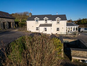 A two-story house with a large front porch and a garage. - Crogal Farmhouse (New Quay)