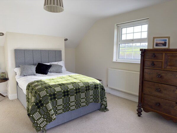 A bedroom with a bed, a dresser, a window, and a radiator. - Crogal Farmhouse (New Quay)