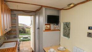 Eine kompakte Küche mit Holzschränken, einem integrierten Fernseher und einem Essbereich mit Tisch für zwei Personen.
