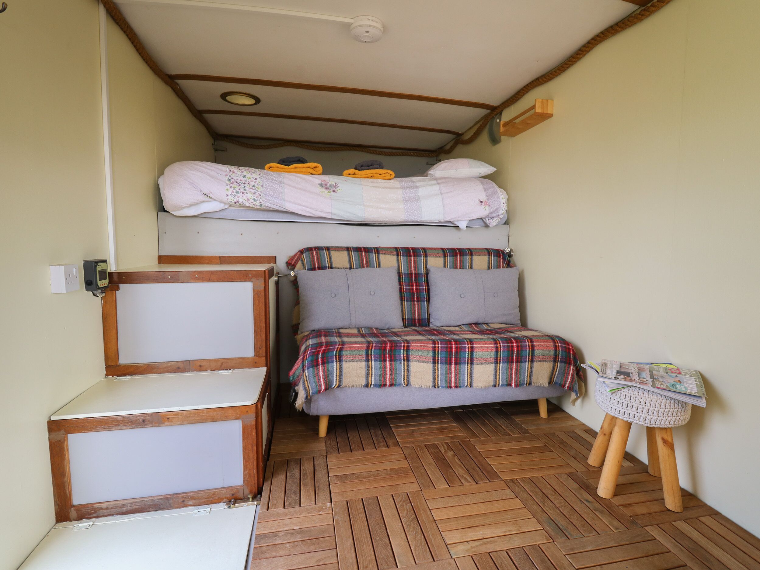 Habitación pequeña con una litera, una cama individual, un taburete de madera y un armario blanco.
