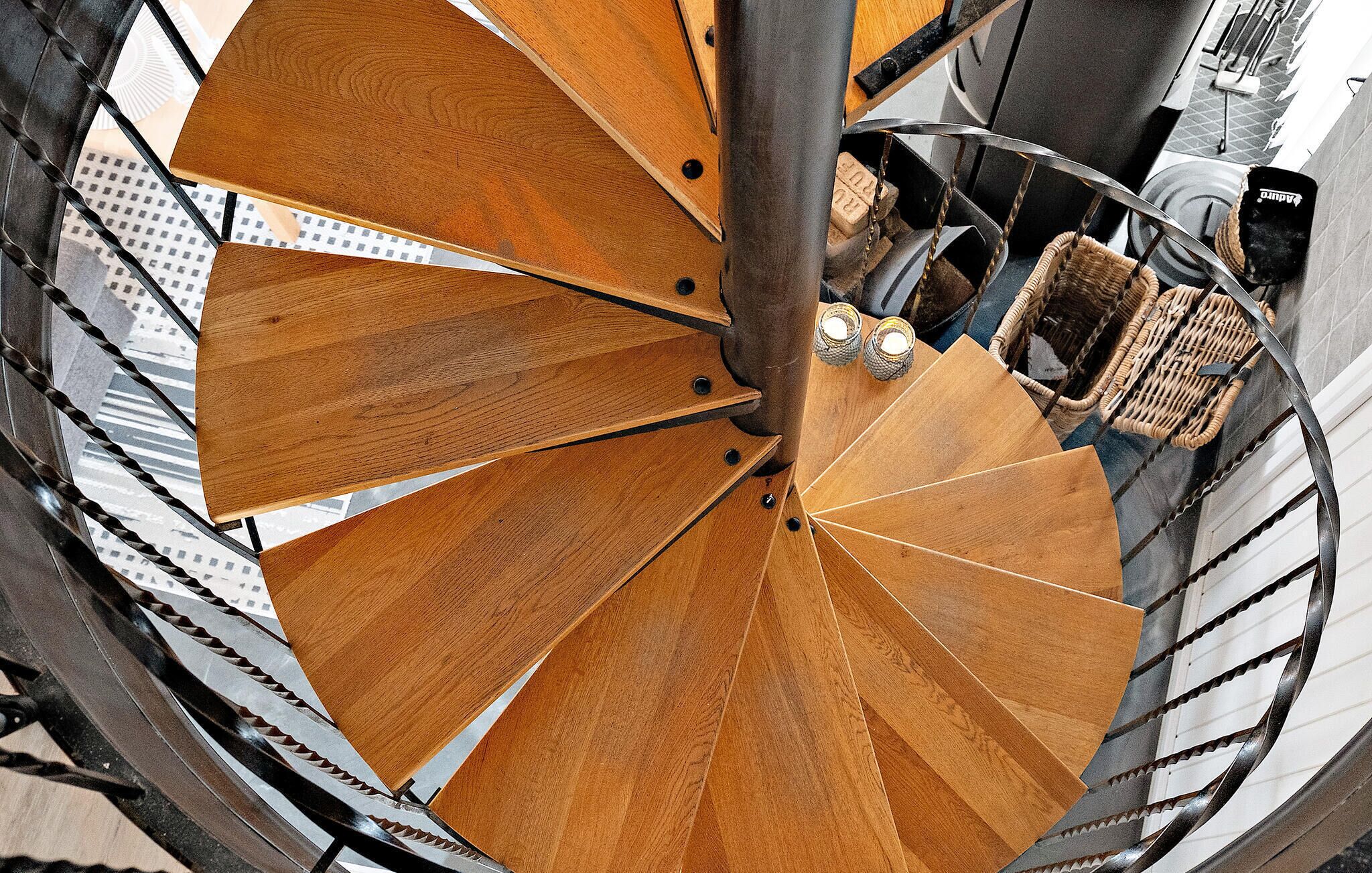 Una escalera de caracol con escalones de madera y barandillas de metal, que sube a un piso superior.