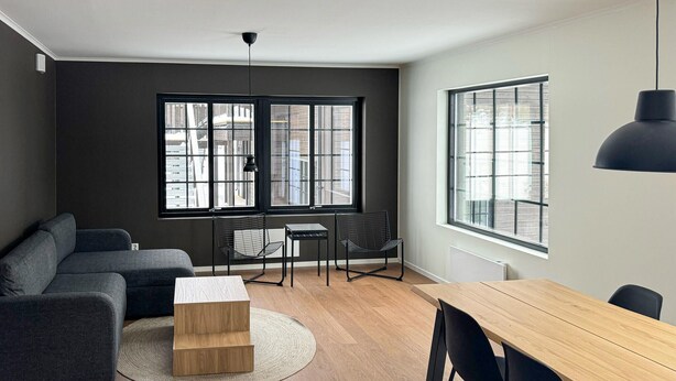 A modern living room with a sofa, a wooden coffee table, a dining table with chairs, and two black chairs. There are large windows with black frames, a hanging light fixture, and a radiator on the wall. - Stunning apartment in Idre with sauna (Idre)